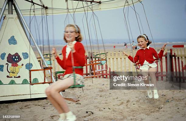 sisters on swing at beach funfair - sixties stockfoto's en -beelden