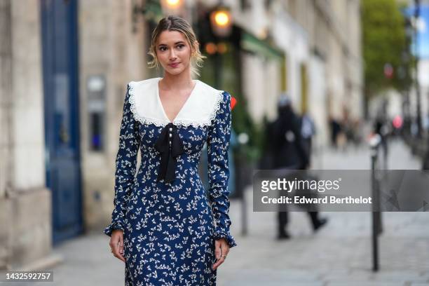 Guest wears gold earrings, a navy blue with white butterfly print pattern / white large collar / long sleeves / long dress, a black knot tie, outside...