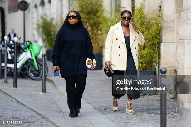 Guest wears black square sunglasses, a black turtleneck oversized pullover, black pants, black suede pointed pumps heels shoes, a white pleated /...