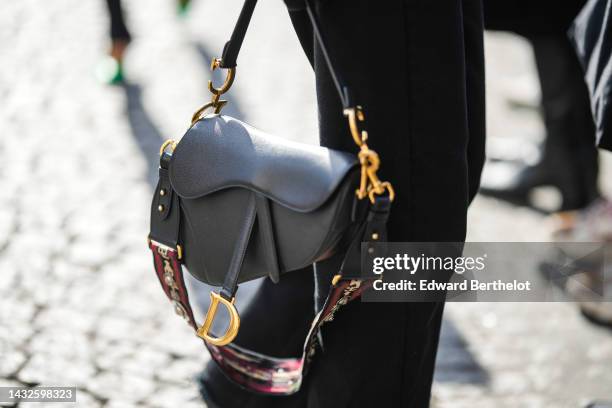 Guest wears black denim ripped wide legs pants, a black shiny leather Saddle handbag from Dior with a matching western strap from Dior, outside...