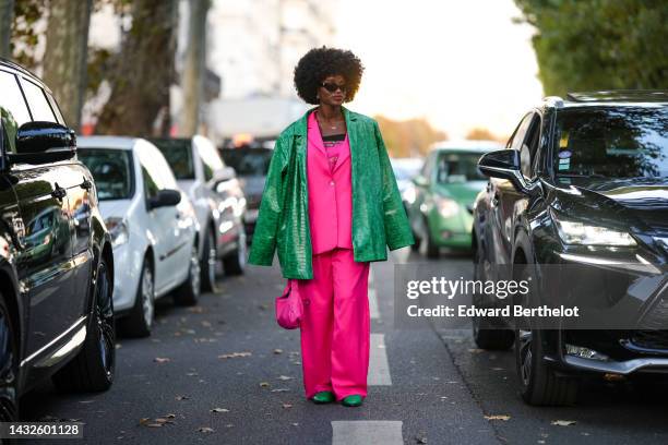 Guest wears black sunglasses, gold earrings, a gold chain necklace, a neon pink with gold and silver print pattern shoulder-off top, a neon pink...