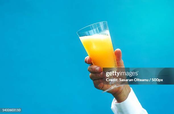 cropped hand holding juice against blue background - orange juice glass white background stock-fotos und bilder