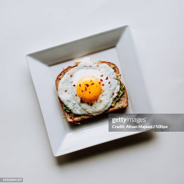 fried egg on a white plate with brown bread - square plate stock-fotos und bilder