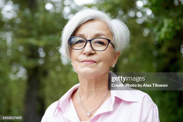 head shot portrait attractive grey-haired older woman wear glasses standing alone in the summer park - baby boomer stock-fotos und bilder