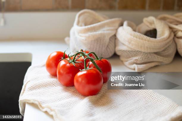 bunch of tomatoes on vine with reusable produce bags - tomaten stock-fotos und bilder