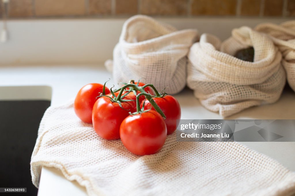 Bunch of tomatoes on vine with reusable produce bags