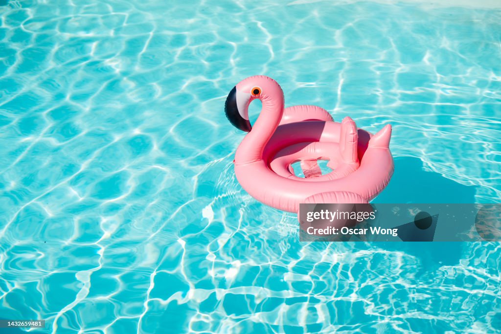 A pink inflatable flamingo float on blue water in the swimming pool with sunlight