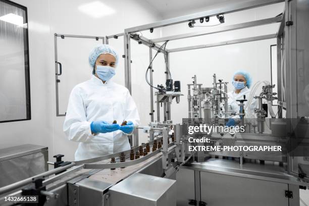 two fully equipped coworkers in protective workwear seen in a pharmaceutical laboratory - biotech industries images stock pictures, royalty-free photos & images