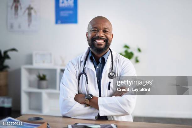 medizinischer, porträt- und afrikanischer arzt, der mit einem lächeln an einem tisch in seinem büro in einem krankenhaus beratend ist. schwarzer mann, chirurg oder kardiologe mit stolz und verschränkten armen, während er in einer klinik arbeitete - doctor smile stock-fotos und bilder