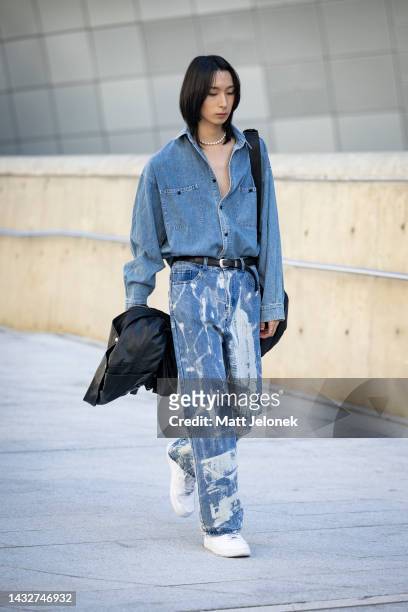 Guest wears a denim shirt with bleach splattered jeans and white sneakers outside Dongdaemun Design Plaza at Seoul Fashion Week SS 23 on October 12,...
