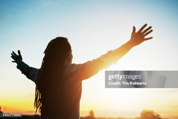 man with arms outstretched at sunset - pregare foto e immagini stock