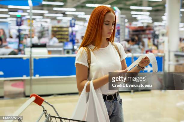 women shopping at the supermarket and looks at receipt total - bonnetje stockfoto's en -beelden