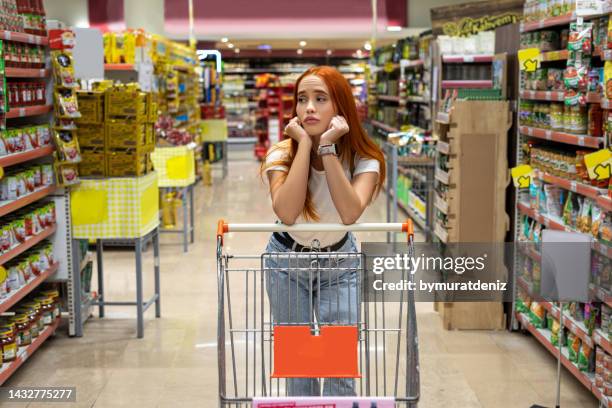 upset woman in a supermarket looking - shopping trolleys stockfoto's en -beelden