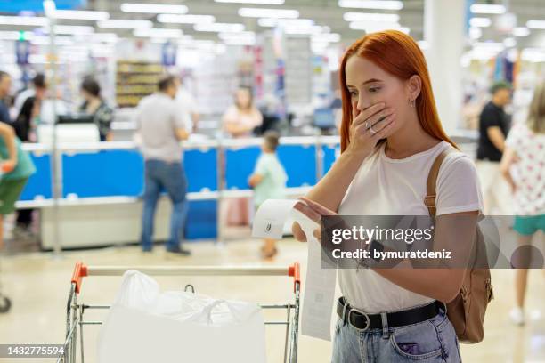 surprised woman looks at receipt total with food in mall - cost of shopping stock pictures, royalty-free photos & images