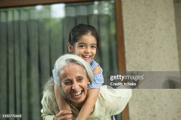 grandmother piggybacking granddaughter at home - indian grandparents stock pictures, royalty-free photos & images