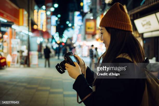 young asian female traveller taking pictures with camera while exploring and strolling in busy local city street at night in osaka, japan. travel, vacation and holiday concept - street market stock pictures, royalty-free photos & images