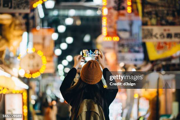 rear view of asian female traveller photographing the vitality and colourful neon signboards of busy downtown city street scene with smartphone while travelling and exploring in osaka, japan. travel, vacation and holiday concept - osaka city 個照片及圖片檔