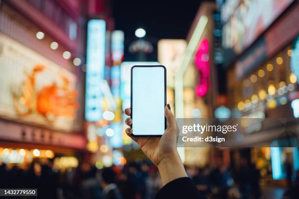 cropped hand of woman holding up smartphone against popular nightlife and entertainment area at night in osaka, japan. a tourist destination with illuminated signboards. mobile phone with blank screen for design mockup. travel, vacation and technology - smartphone hand ストックフォトと画像