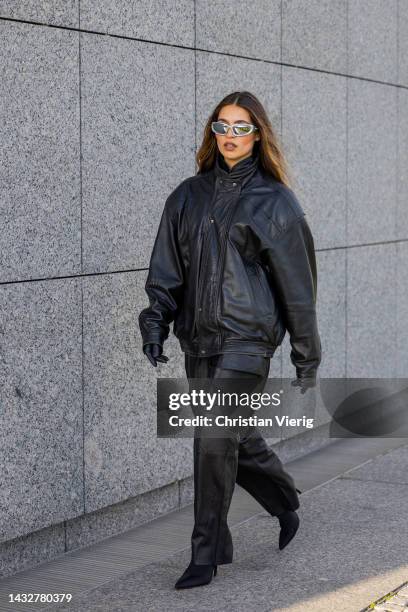 Isaya Elias wears black leather bomber jacket, gloves, Balenciaga sunglasses, overall with side pockets, heeled ankle boots on October 11, 2022 in...