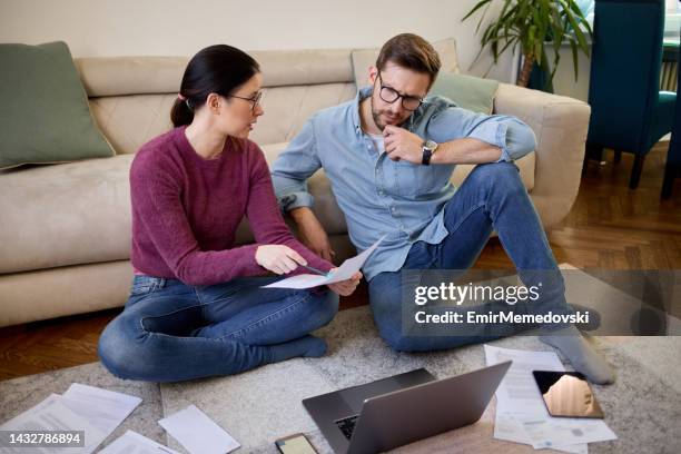 couple sitting in their living room and checking their finances using laptop - mid adult couple stock pictures, royalty-free photos & images
