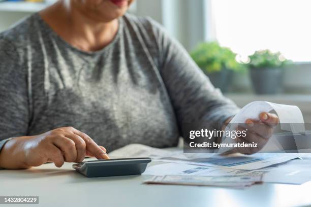 mujer madura revisando sus facturas de energía en la mesa - costo de vida fotografías e imágenes de stock