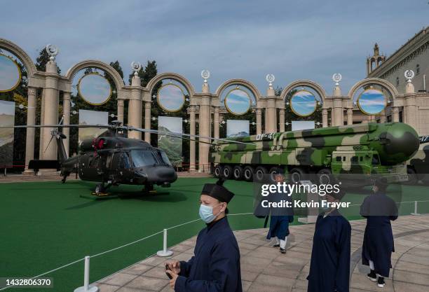 Party members wear traditional religious robes as they look at a helicopter and missile launcher as part of a display of military hardware at an...