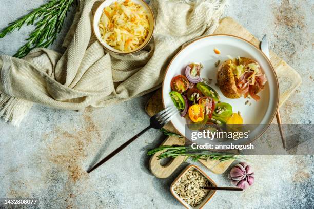 overhead view of a half eaten baked potato stuffed with bacon and cabbage and a tomato, red onion, chilli pepper and sunflower seed salad - foodstyling stock-fotos und bilder