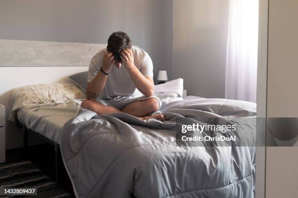 portrait of a man sitting on a bed with his head in his hands - hopelessness stock-fotos und bilder