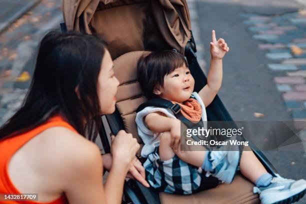 young asian mother putting her toddler girl on pushchair in the city - baby in stroller stock pictures, royalty-free photos & images