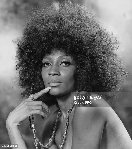 Woman with an afro hairstyle, wearing a long shell necklace, holding her finger to her lip with bare shoulders, United States, circa 1975.