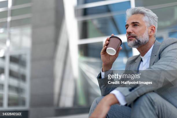 businessman in suit sitting outdoor in city and drinking coffee. - gray suit stock pictures, royalty-free photos & images