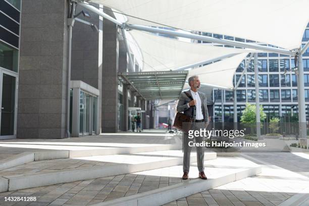mature businessman walking outside office building in city. - executive producer stockfoto's en -beelden