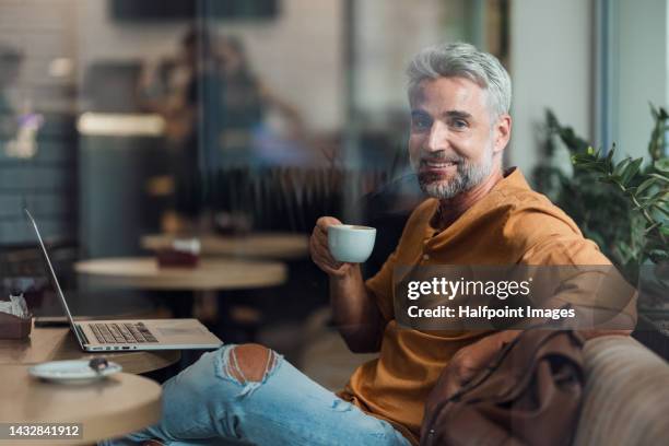 mature man sitting at cafe with his laptop, remote office concept. - 40s laptop stock-fotos und bilder