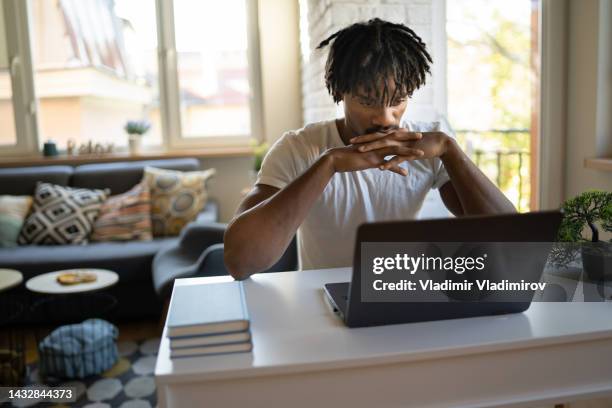 an african-american young man is watching an online lesson on his laptop - avondschool stockfoto's en -beelden