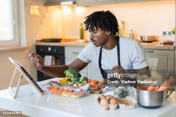 man using a digital tablet for recipe ideas in a kitchen - watching youtube stock pictures, royalty-free photos & images