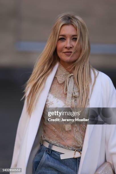 Tanja Comba is seen wearing beige/gold lace blouse from Valentino, blue denim pants from Khaite, creme white long knit cardigan/coat from Roberto...