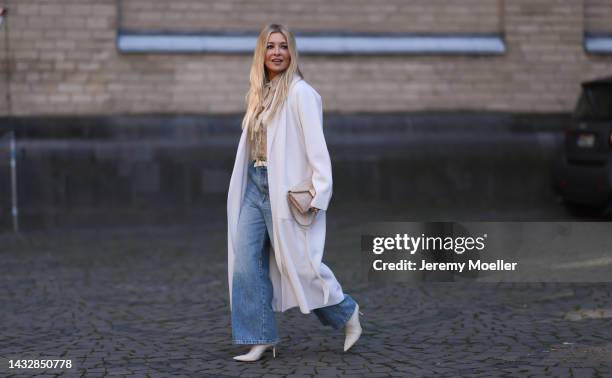 Tanja Comba is seen wearing beige/gold lace blouse from Valentino, blue denim pants from Khaite, creme white long knit cardigan/coat from Roberto...