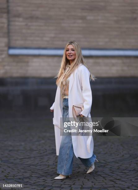 Tanja Comba is seen wearing beige/gold lace blouse from Valentino, blue denim pants from Khaite, creme white long knit cardigan/coat from Roberto...