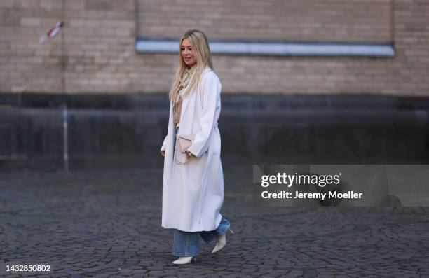 Tanja Comba is seen wearing beige/gold lace blouse from Valentino, blue denim pants from Khaite, creme white long knit cardigan/coat from Roberto...