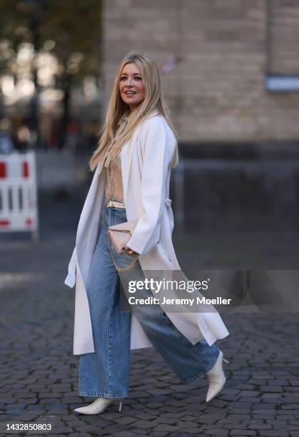 Tanja Comba is seen wearing beige/gold lace blouse from Valentino, blue denim pants from Khaite, creme white long knit cardigan/coat from Roberto...