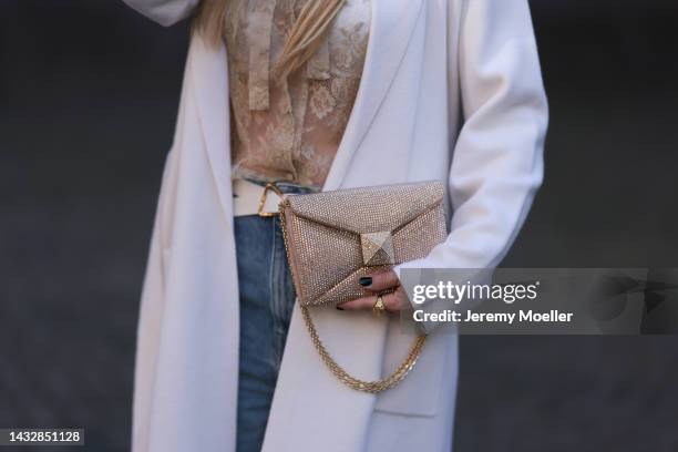 Tanja Comba is seen wearing beige/gold lace blouse from Valentino, blue denim pants from Khaite, creme white long knit cardigan/coat from Roberto...