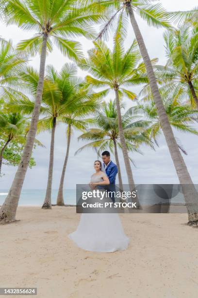 the groom and the bride are on the beach with many coconut trees and the sea in the background. - beach wedding stock pictures, royalty-free photos & images