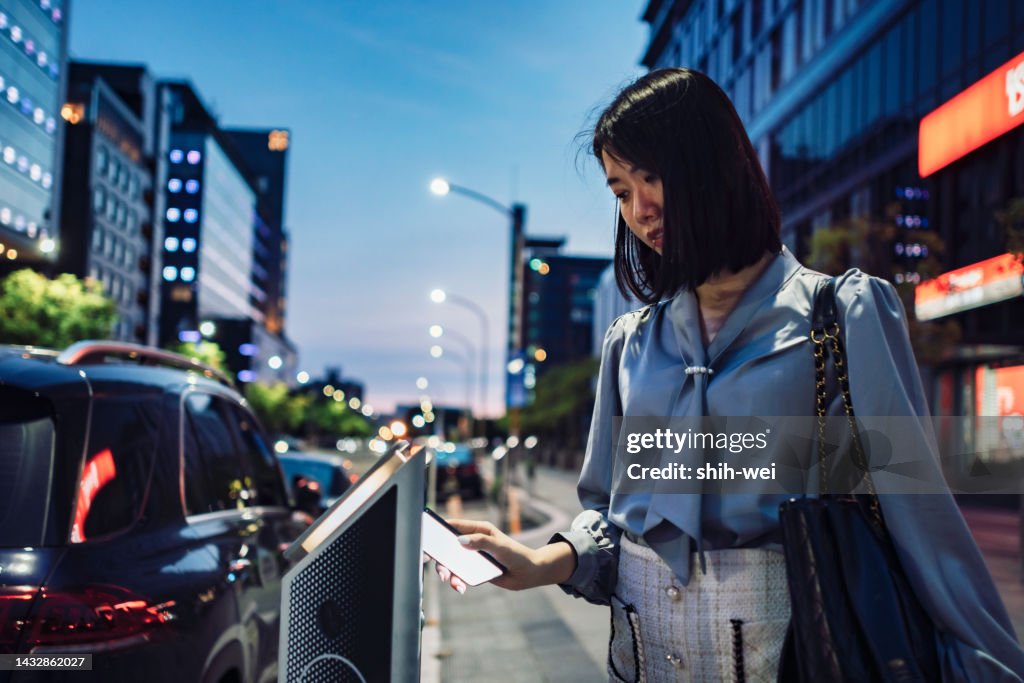 Asian business woman in the city making mobile payment for parking place