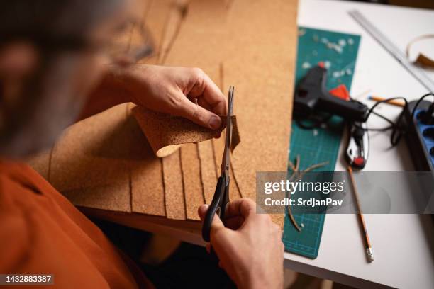 architetto maschio irriconoscibile che taglia il sughero con le forbici mentre realizza un modello architettonico - sughero foto e immagini stock