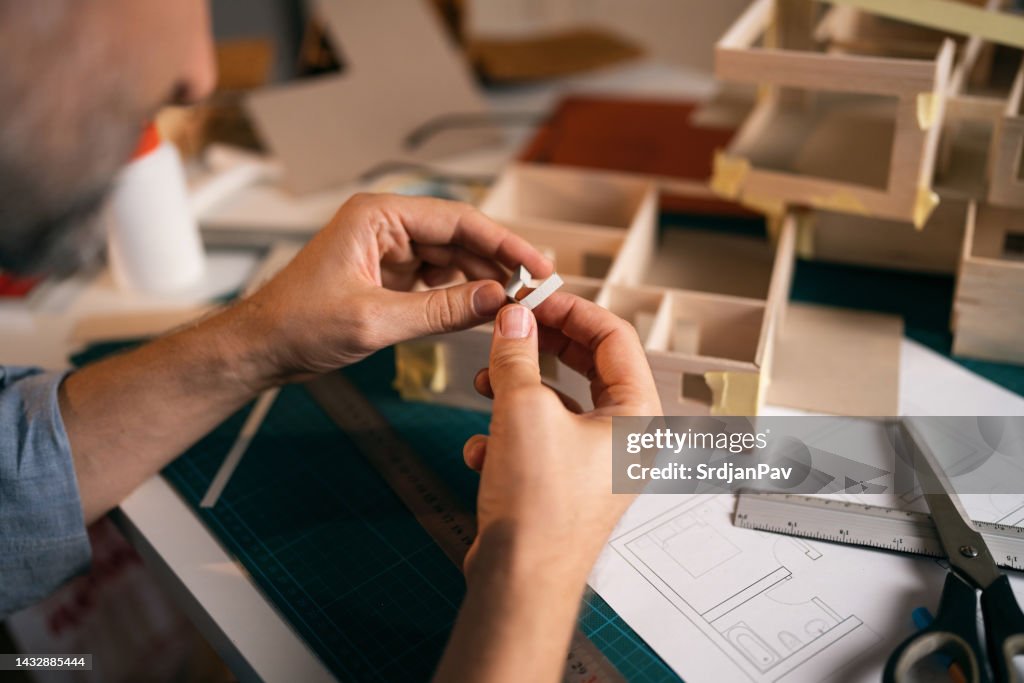Nicht erkennbarer Architekt biegt ein kleines Stück Papier, während er ein Architekturmodell erstellt