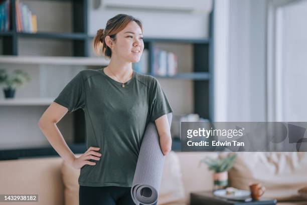 portrait chinese woman with disability deformed arm holding yoga matt looking at camera - amputee home stock pictures, royalty-free photos & images