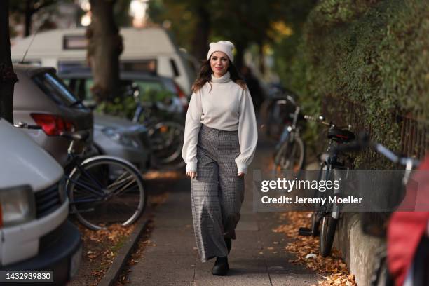 Anna Wolfers wearing a cream knit hat, cream turtleneck sweater, plaid brown trousers and black boots on October 06, 2022 in Hamburg, Germany.