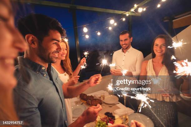 gruppo di amici che tengono scintille e condividono un pasto e un drink di champagne all'aperto - cena capodanno foto e immagini stock