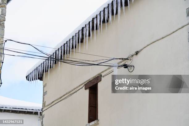 wall of a building with a roof which overhangs a little and from it hang some pieces of ice in a conical shape, at a certain height of the wall cables can be seen. - conical roof stock pictures, royalty-free photos & images