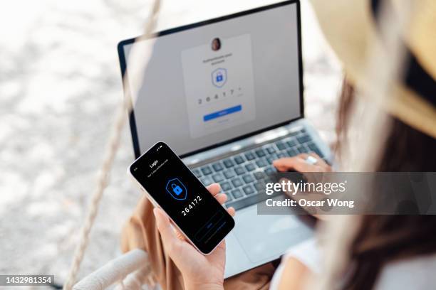 over the shoulder view of young woman logging onto online bank account with laptop and smart phone while having vacation - passwords stockfoto's en -beelden